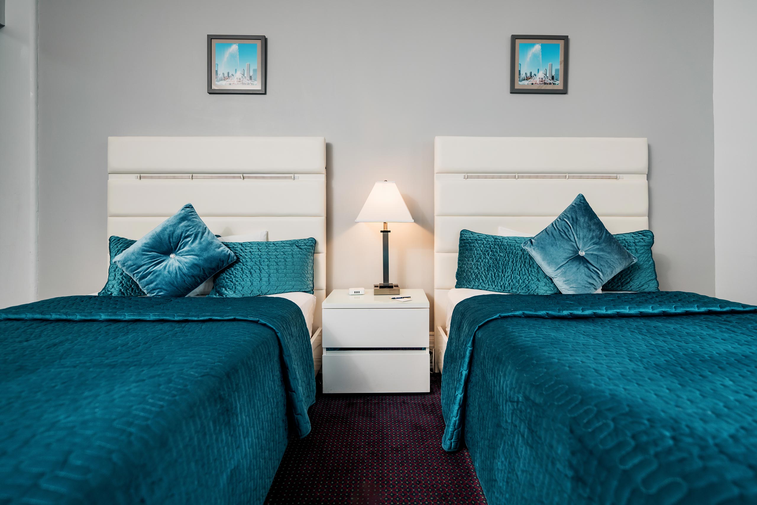 Two beds with blue pillows and picture hanging on wall
